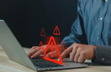 A photo of a person on a laptop with warning signs (triangle with exclamation points) coming from the computer